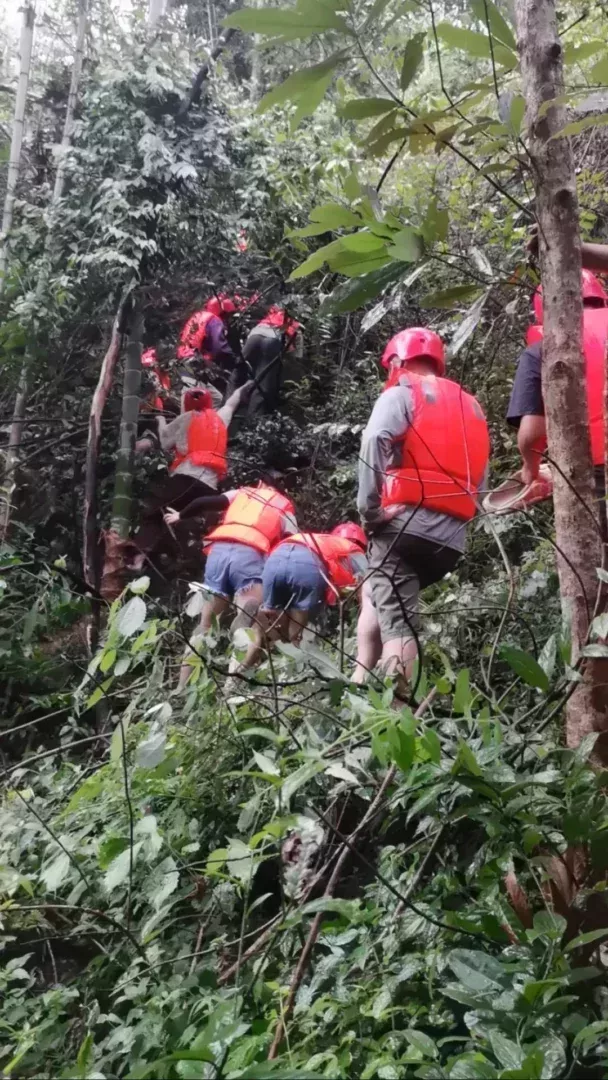 ▲原始山林裏沒有路,遊客們依次排開,拽着樹枝往上爬,由於道路陡峭溼滑,很多人脫了鞋赤腳爬山。受訪者供圖