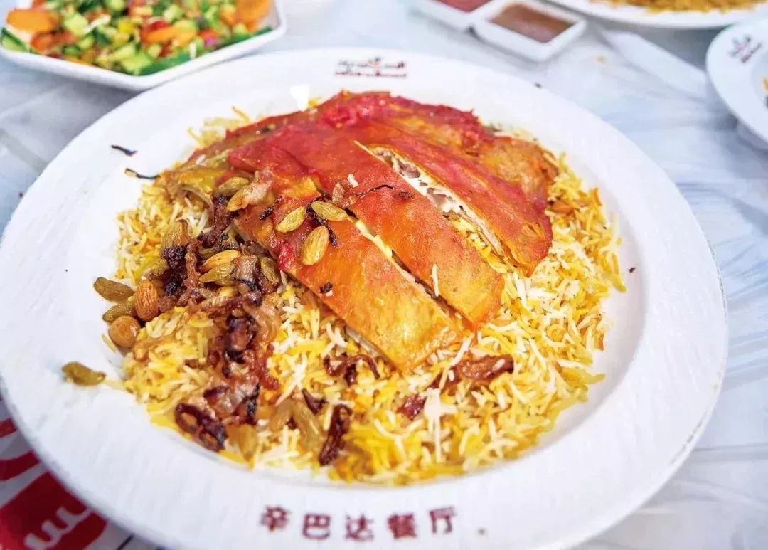 一盤也門羊肉抓飯。羊肉的調料汁混合油脂,將米飯染成了橘紅色